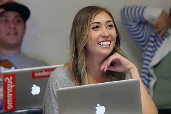  student with laptop smiling in classroom