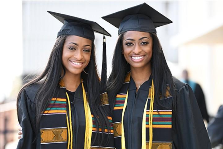 Two graduates wearing caps and gowns smiling