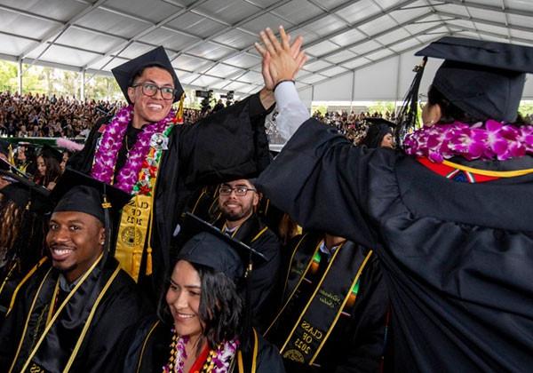 Students at graduation ceremony give each other high-fives.